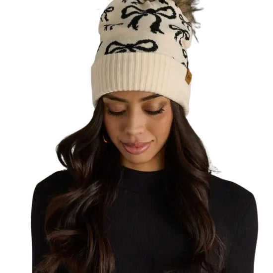 Woman wearing a cream beanie with black bows on a white background