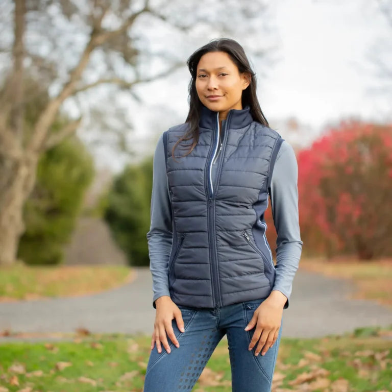 Woman wearing a blue Equinavia Insulated vest outdoors with blurred trees and foliage in the background