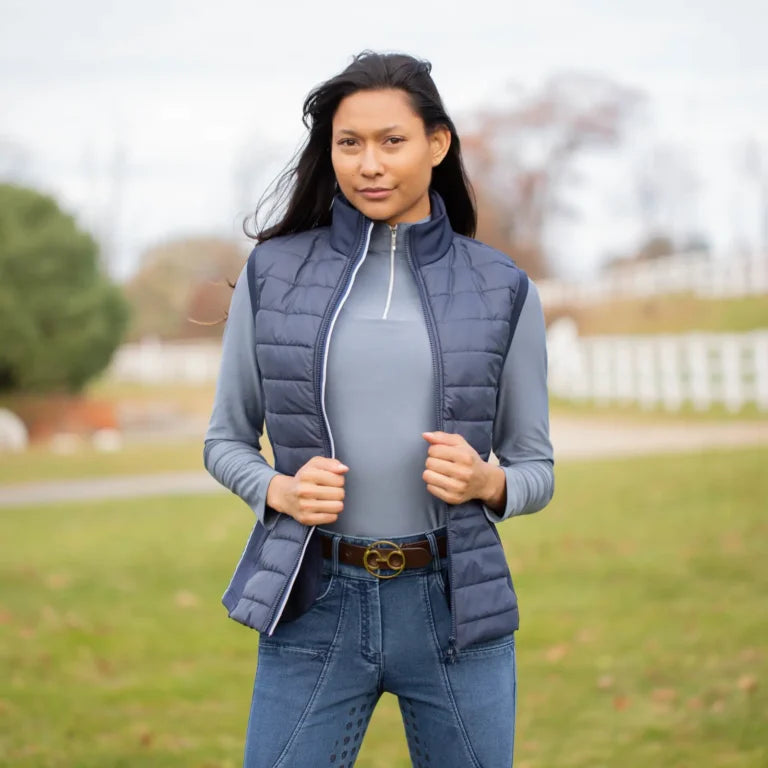 Woman wearing a blue Equinavia Insulated vest outdoors with blurred trees and foliage in the background