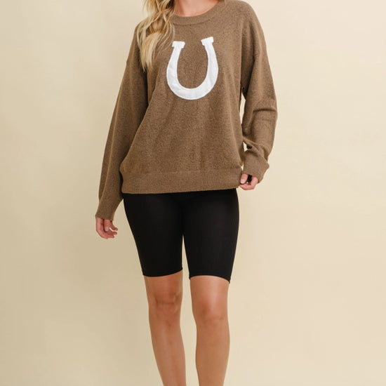 Woman wearing a brown sweater with a white horseshoe design on a beige background - equestrian fashion outfitters