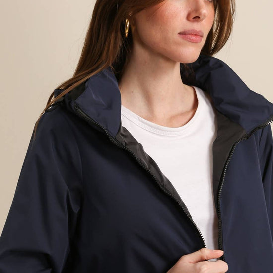 Woman wearing a navy blue jacket over a white shirt against a beige background equestrian fashion outfitters