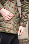 equestrian fashion outfitters - Close-up of a person wearing a green quilted jacket with orange and brown detail.