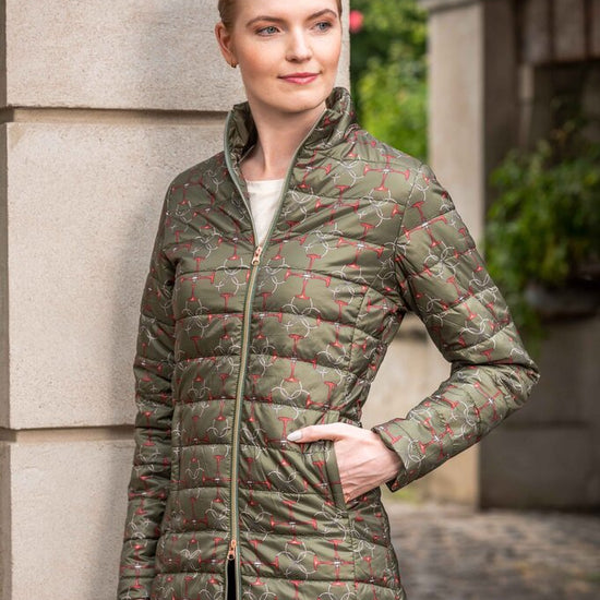 Woman wearing a green quilted jacket with floral pattern standing against a stone wall.