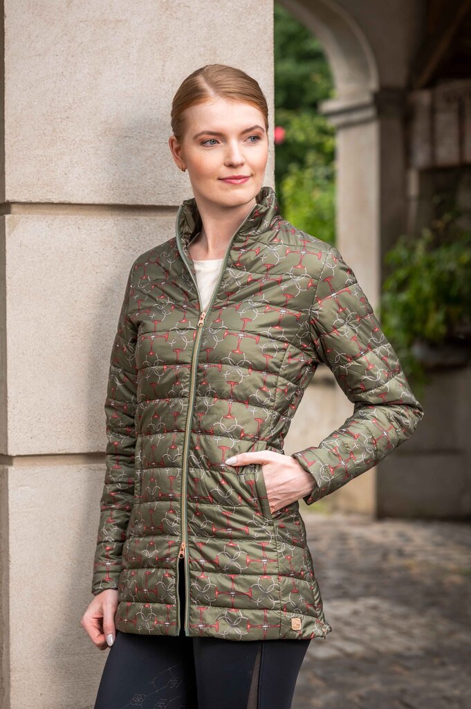Woman wearing a green quilted jacket with floral pattern standing against a stone wall.