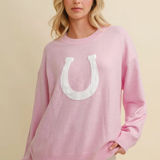 Woman wearing a pink horseshoe sweater  on a beige background - equestrian fashion outfitters