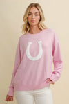Woman wearing a pink horseshoe sweater  on a beige background - equestrian fashion outfitters