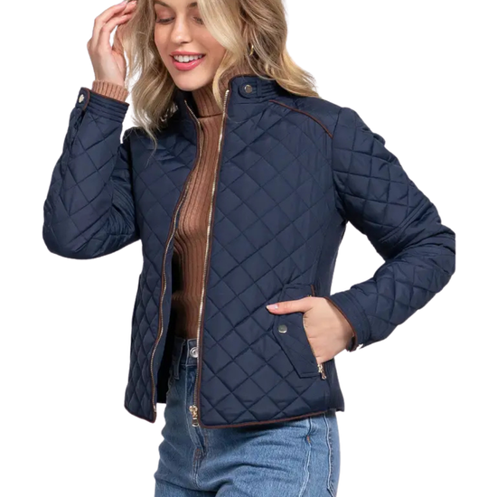 A woman modeling a navy blue diamond-quilted jacket with brown trim over a brown ribbed turtleneck and blue jeans, set against a plain white background equestrian fashion outfitters