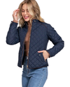A woman modeling a navy blue diamond-quilted jacket with brown trim over a brown ribbed turtleneck and blue jeans, set against a plain white background equestrian fashion outfitters