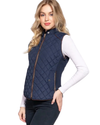 A woman modeling a navy blue quilted sleeveless vest with brown trim over a white long-sleeve top and dark pants, against a plain white background. equestrian fashion outfitters