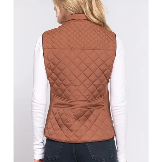 A woman shown from the back wearing a quilted sleeveless vest in a warm rust brown camel color over a white long-sleeve shirt and dark jeans, equestrian fashion outfitters.