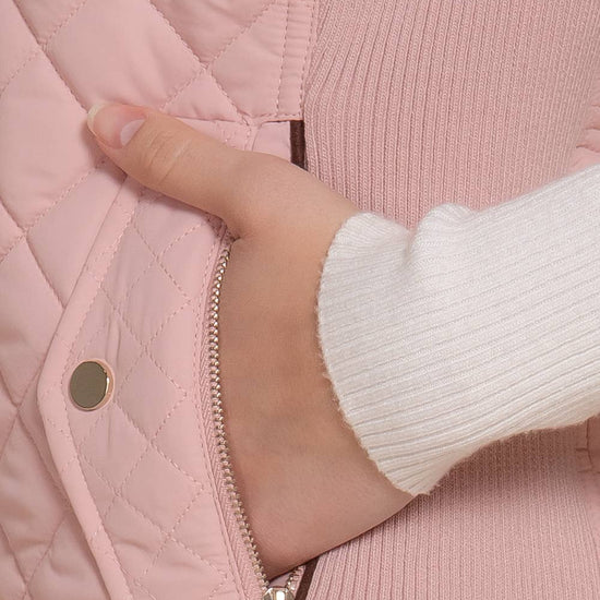 Close-up of a hand opening a pink quilted jacket zipper. equestrian fashion outfitters