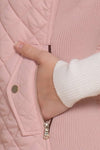 Close-up of a hand opening a pink quilted jacket zipper. equestrian fashion outfitters