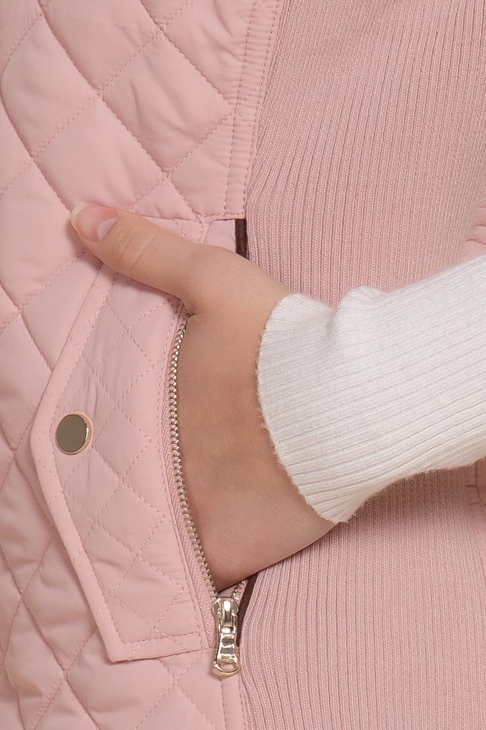 Close-up of a hand opening a pink quilted jacket zipper. equestrian fashion outfitters