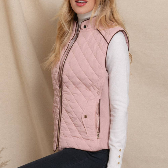 Woman wearing a pink quilted vest against a beige background equestrian fashion outfitters