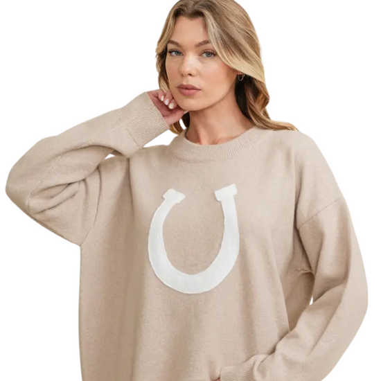 Woman wearing a beige sweater with a white horseshoe design on a white background