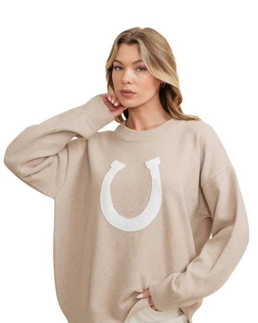 Woman wearing a beige sweater with a white horseshoe design on a white background