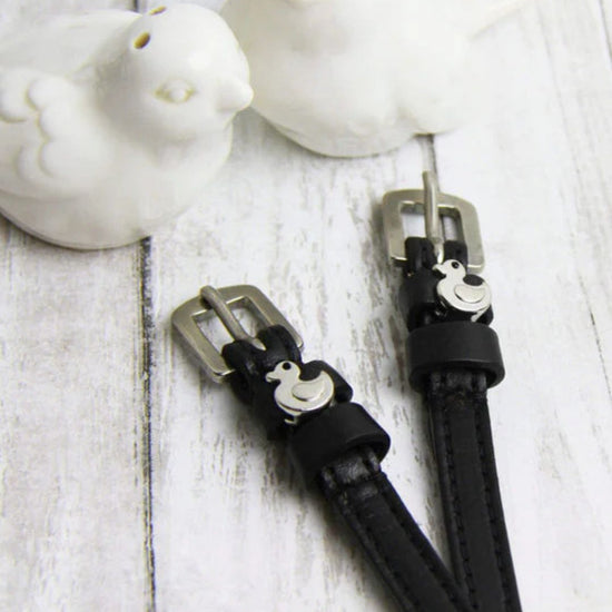 Black Spur Straps with a duck silver buckles on a light wooden surface.