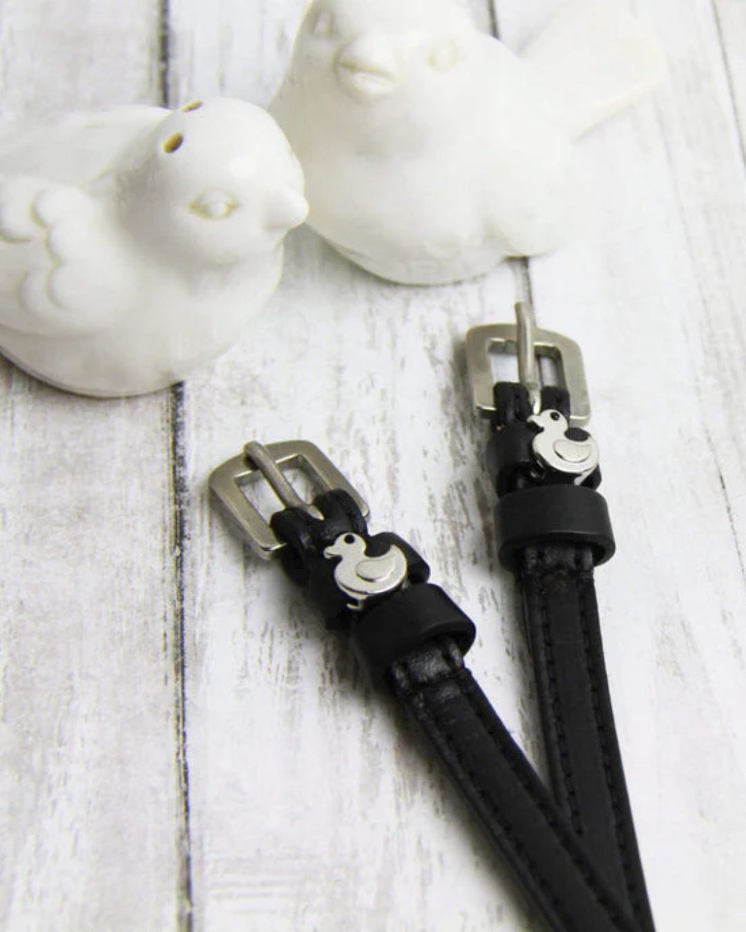 Black Spur Straps with a duck silver buckles on a light wooden surface.