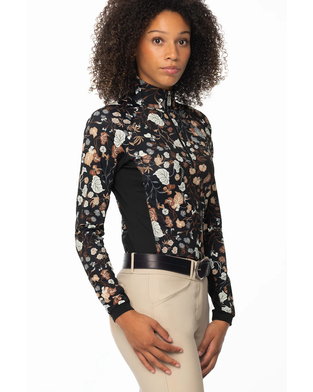 A woman modeling a long-sleeve 1/4 zip equestrian shirt with a black base and a detailed floral and vine pattern in beige, brown, and white, with black side panels paired with beige riding pants equestrian fashion outfitters