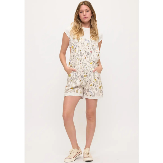 A woman modeling overalls or shortalls with roosters and chickens and flowers on a white background with sneakers equestrian fashion outfitters