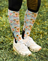 Person wearing floral knee-high socks and white sneakers on grass