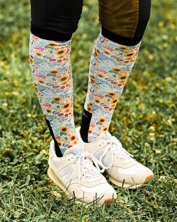 Person wearing floral knee-high socks and white sneakers on grass