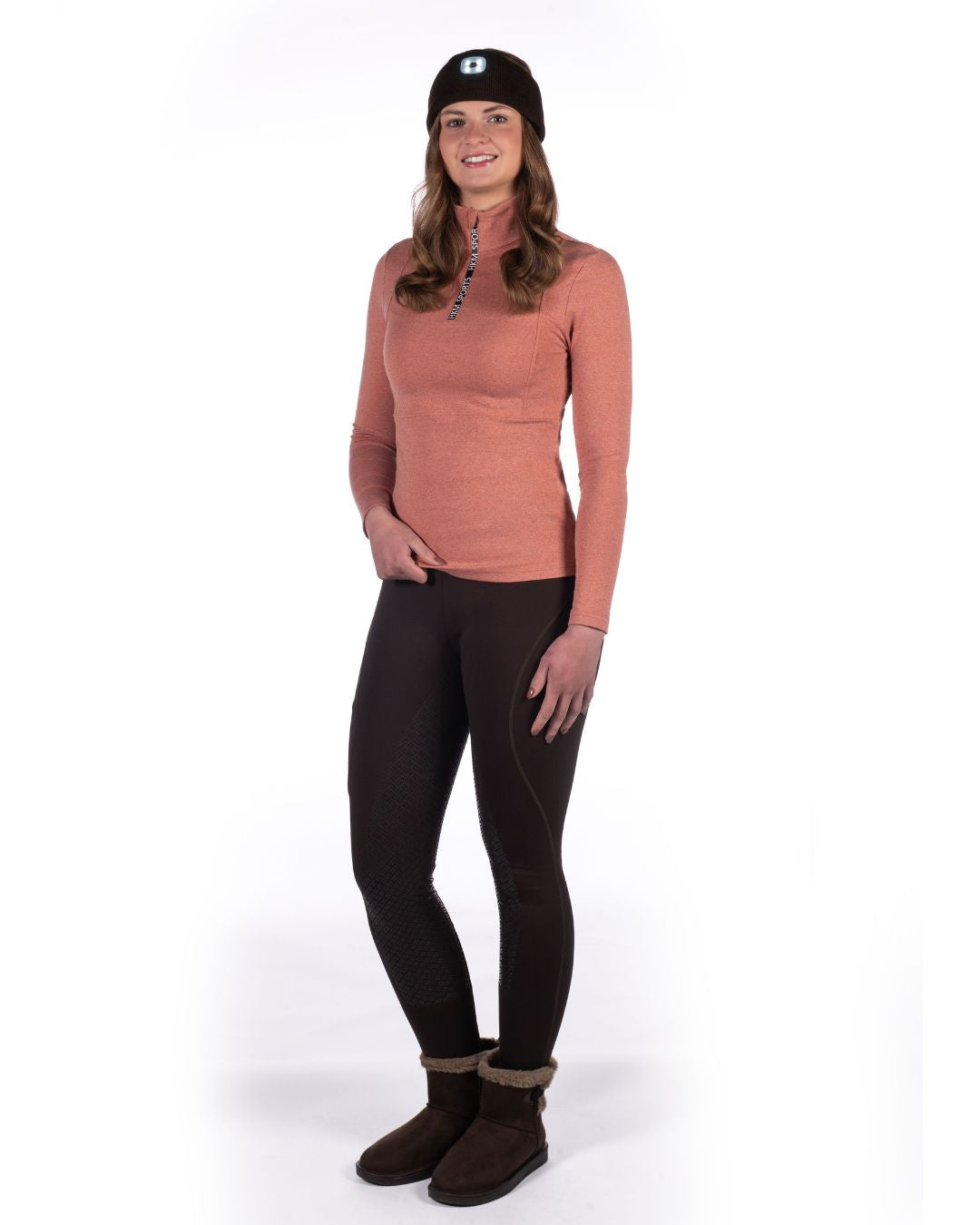 Woman wearing a pink HKM long-sleeve top, HKM black leggings, and brown boots on a white background