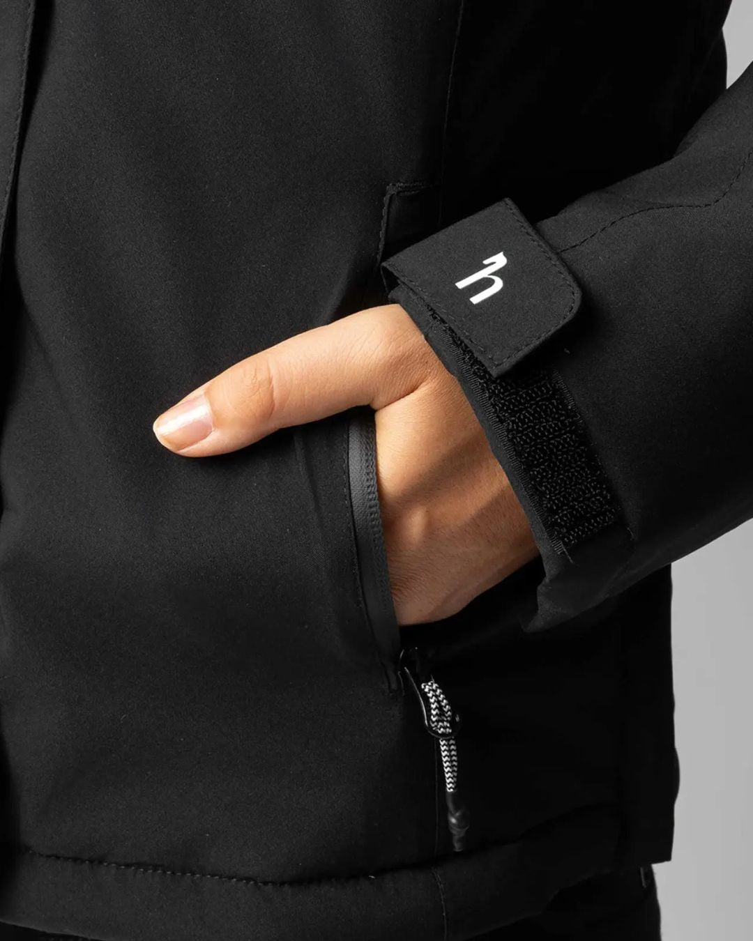 Person wearing a black jacket with hand in pocket on a gray background