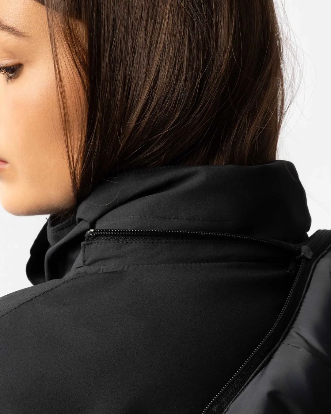 Close-up of a person wearing a black jacket with a detachable hood on a white background