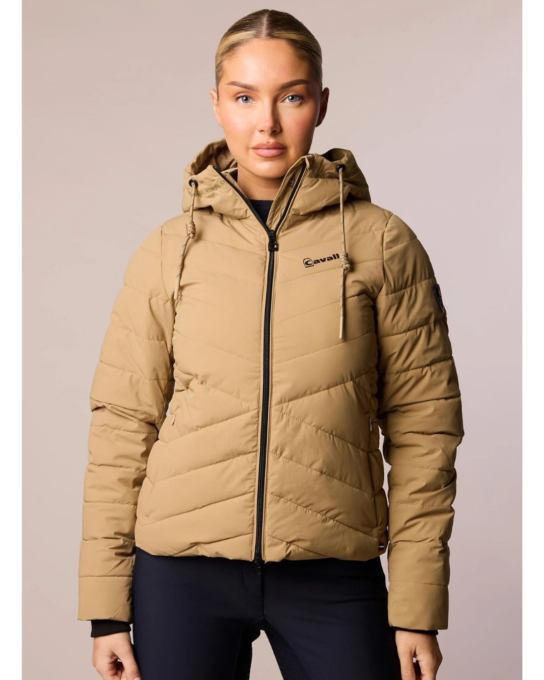 Woman wearing a beige puffer jacket with a brand logo on a plain background