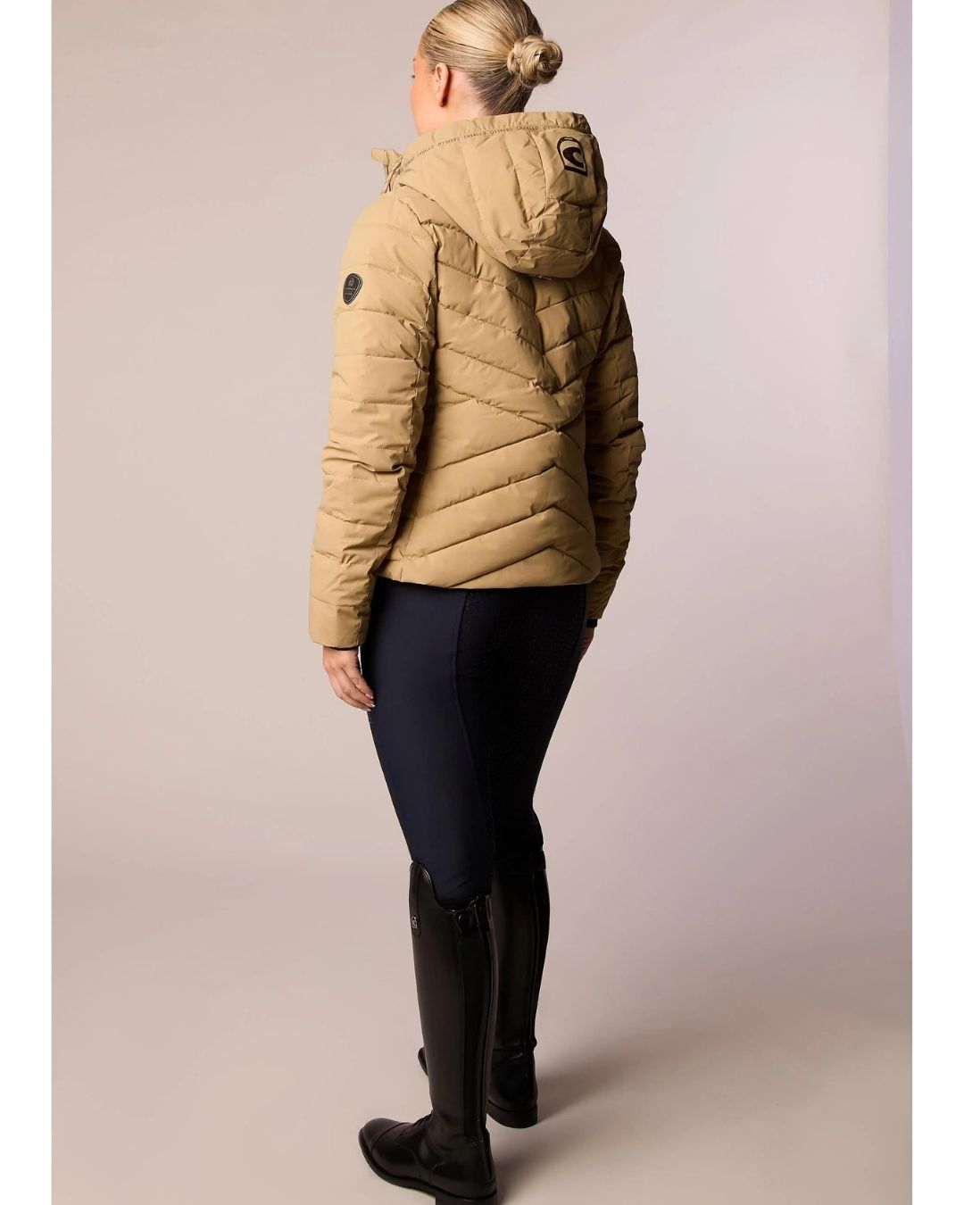 Person wearing a beige puffer jacket and black leggings on a plain background