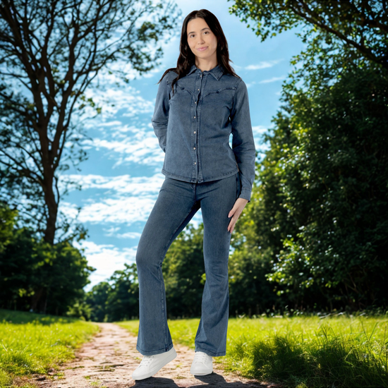 Woman in a denim outfit standing on a path with trees and blue sky in the background