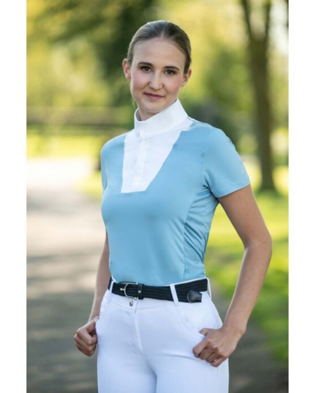 Woman wearing a light blue equestrian shirt with a white collar and white pants outdoors. Equestrian fashion outfitters