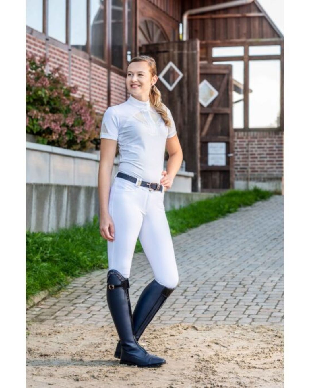 Woman in equestrian attire standing on a path with a building in the background Equestrian fashion outfitters