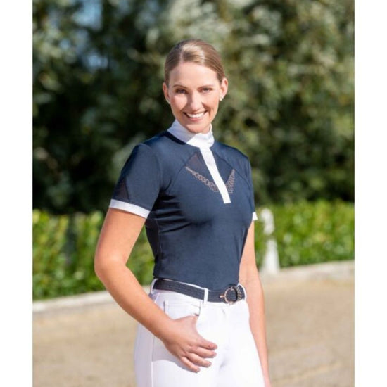 Woman wearing a navy equestrian shirt with white accents and white pants outdoors. Equestrian fashion outfitters