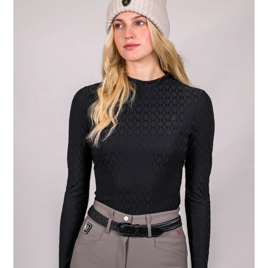 Woman wearing a black long-sleeve top, gray pants, and a white beanie on a gray background