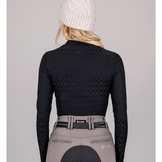 Person wearing a black long-sleeve top and beige riding pants with a white knit cap on a gray background