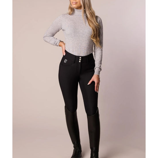 Woman wearing a gray turtleneck and black riding pants on a beige background