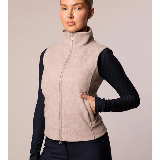 Woman wearing a beige vest over a black long-sleeve shirt on a plain background