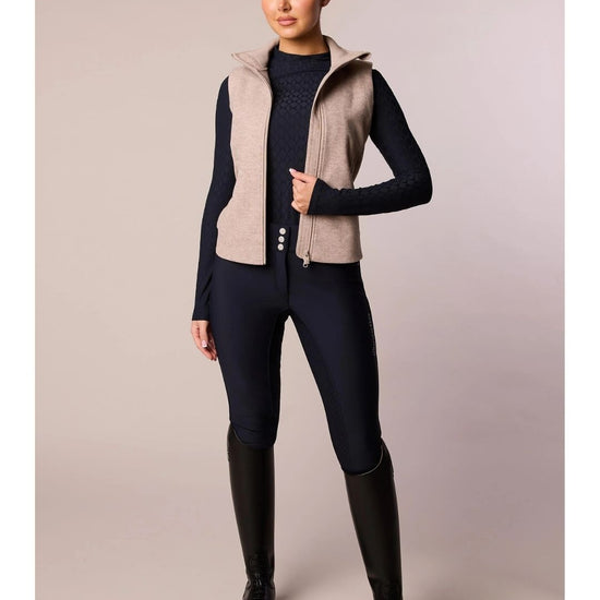 Person wearing equestrian attire with a beige vest and black riding pants on a plain background