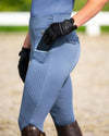 Person wearing blue equestrian pants tights with gloves and boots in an outdoor setting equestrian fashion outfitters