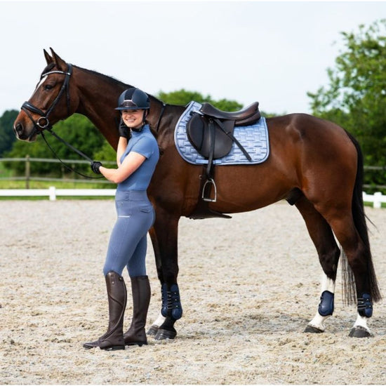 Woman in equestrian attire standing next to a brown horse in an outdoor setting equestrian fashion outfitters
