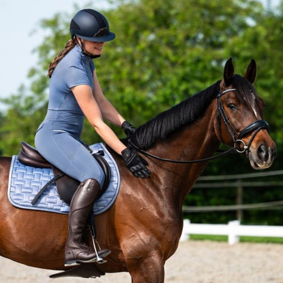 Woman riding a brown horse in an outdoor equestrian setting grey blue tights equestrian fashion outfitters