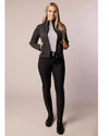 Woman wearing a gray black jacket, gray top, black riding pants, and black boots on a beige background