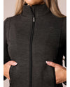 Person wearing a black dark grey zip-up jacket with a visible brand logo on a neutral background