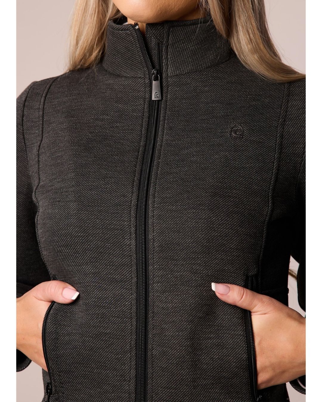 Person wearing a black dark grey zip-up jacket with a visible brand logo on a neutral background