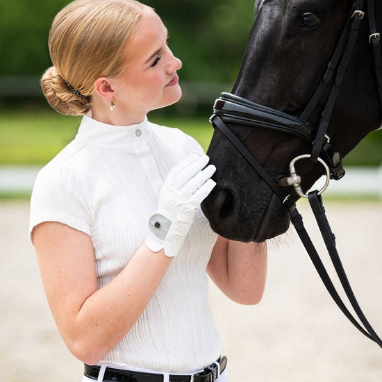 Woman in equestrian qhp show shirt short sleeve petting a black horse in an outdoor setting equestrian fashion outfitters