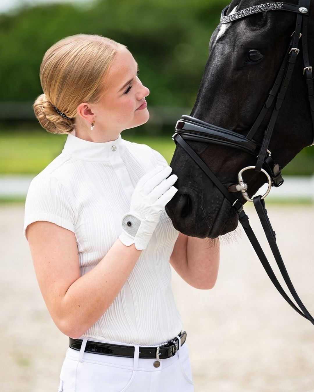 Woman in equestrian qhp show shirt short sleeve petting a black horse in an outdoor setting equestrian fashion outfitters