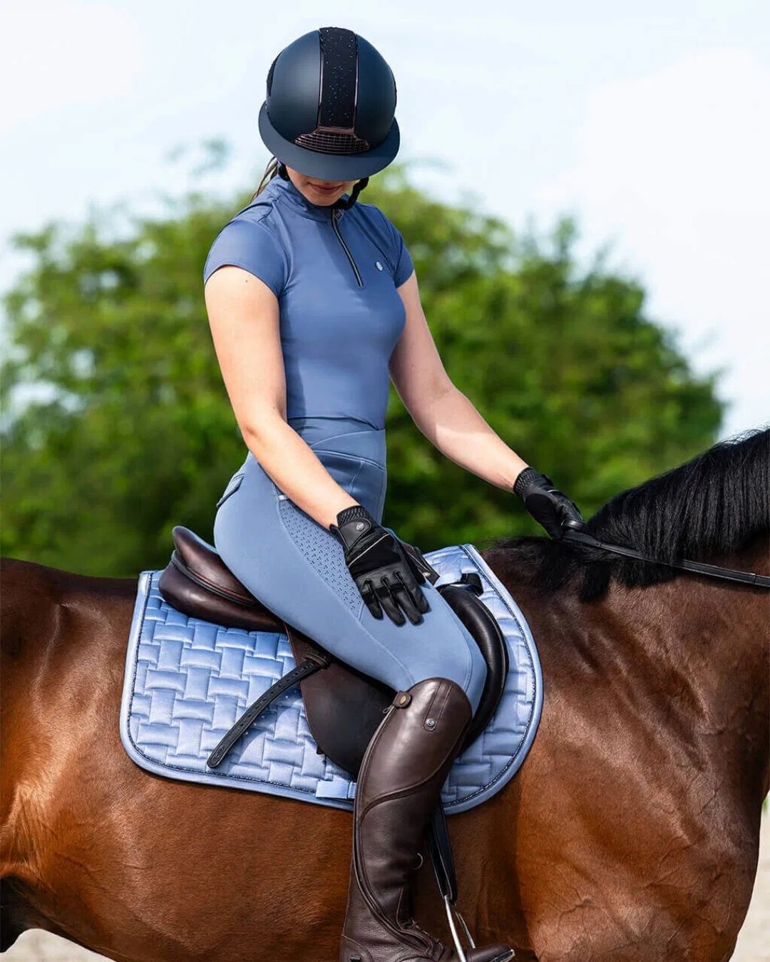 Person in blue qhp training equestrian attire sitting on a horse with a blue saddle pad equestrian fashion outfitters