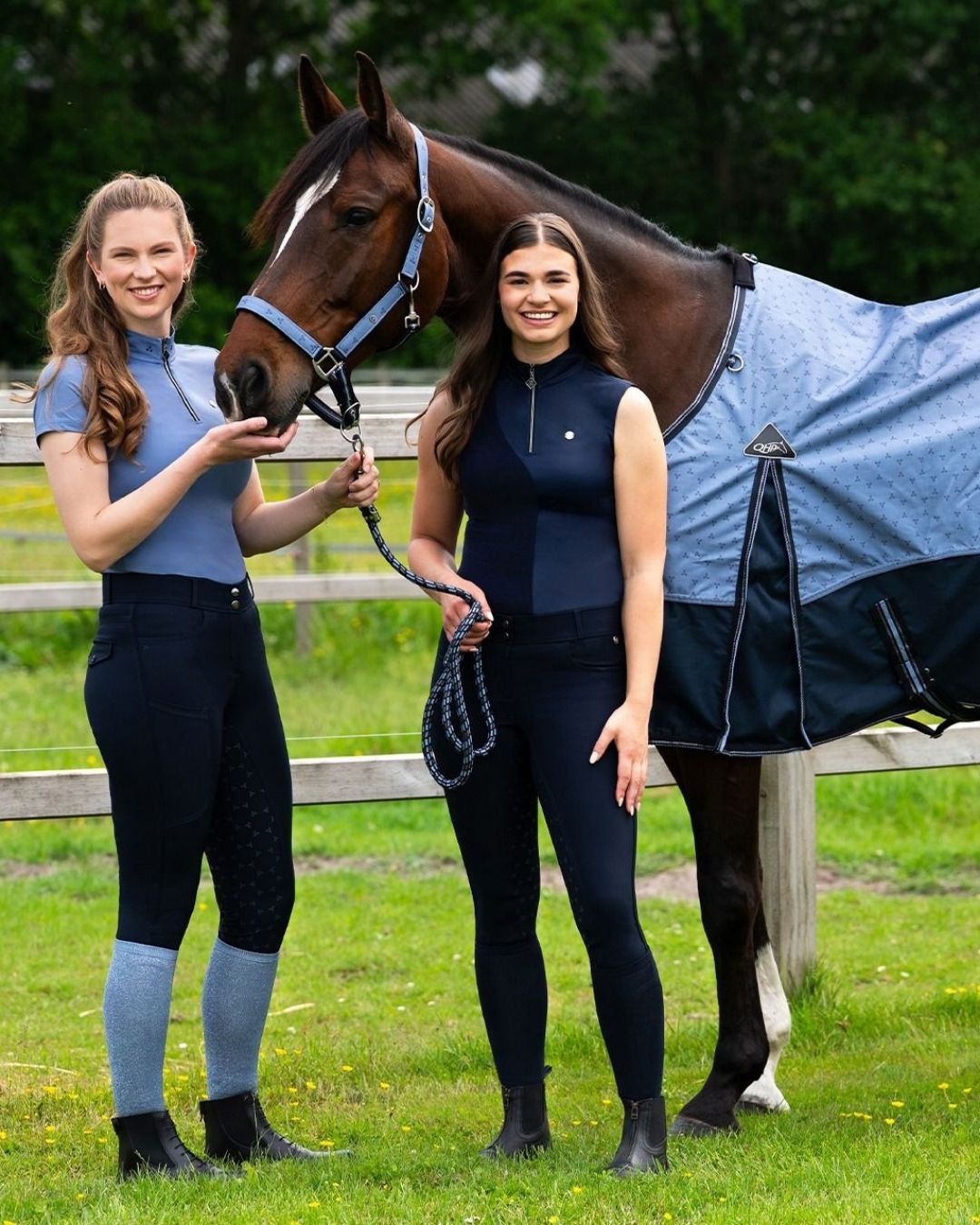 Two women in equestrian attire standing next to a horse with a blue blanket in an outdoor setting qhp aubree shirt and breeches equestrian fashion outfitters